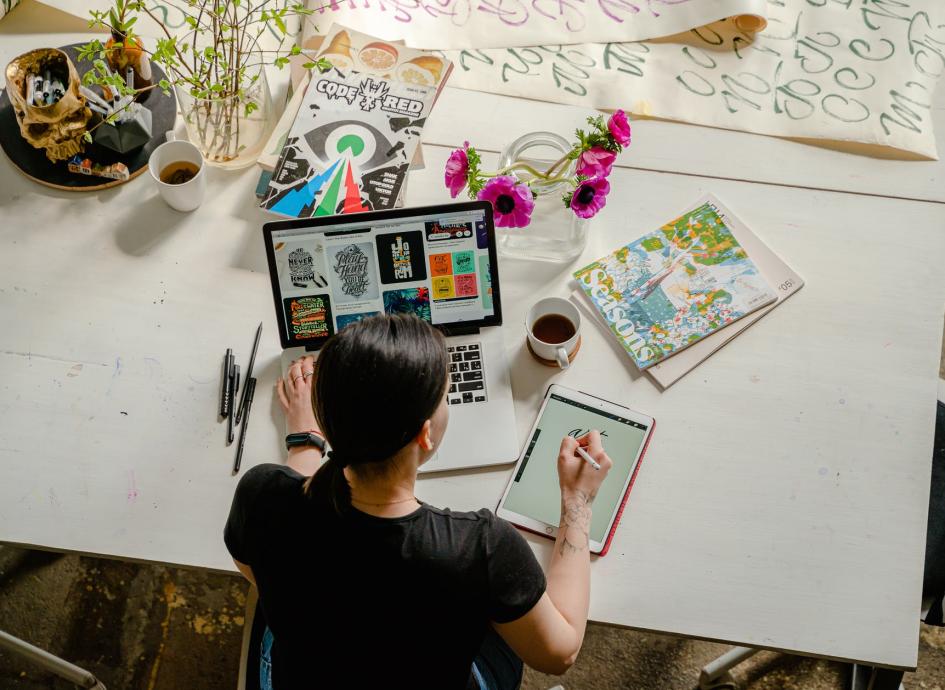 photo of woman writing on tablet computer while using laptop